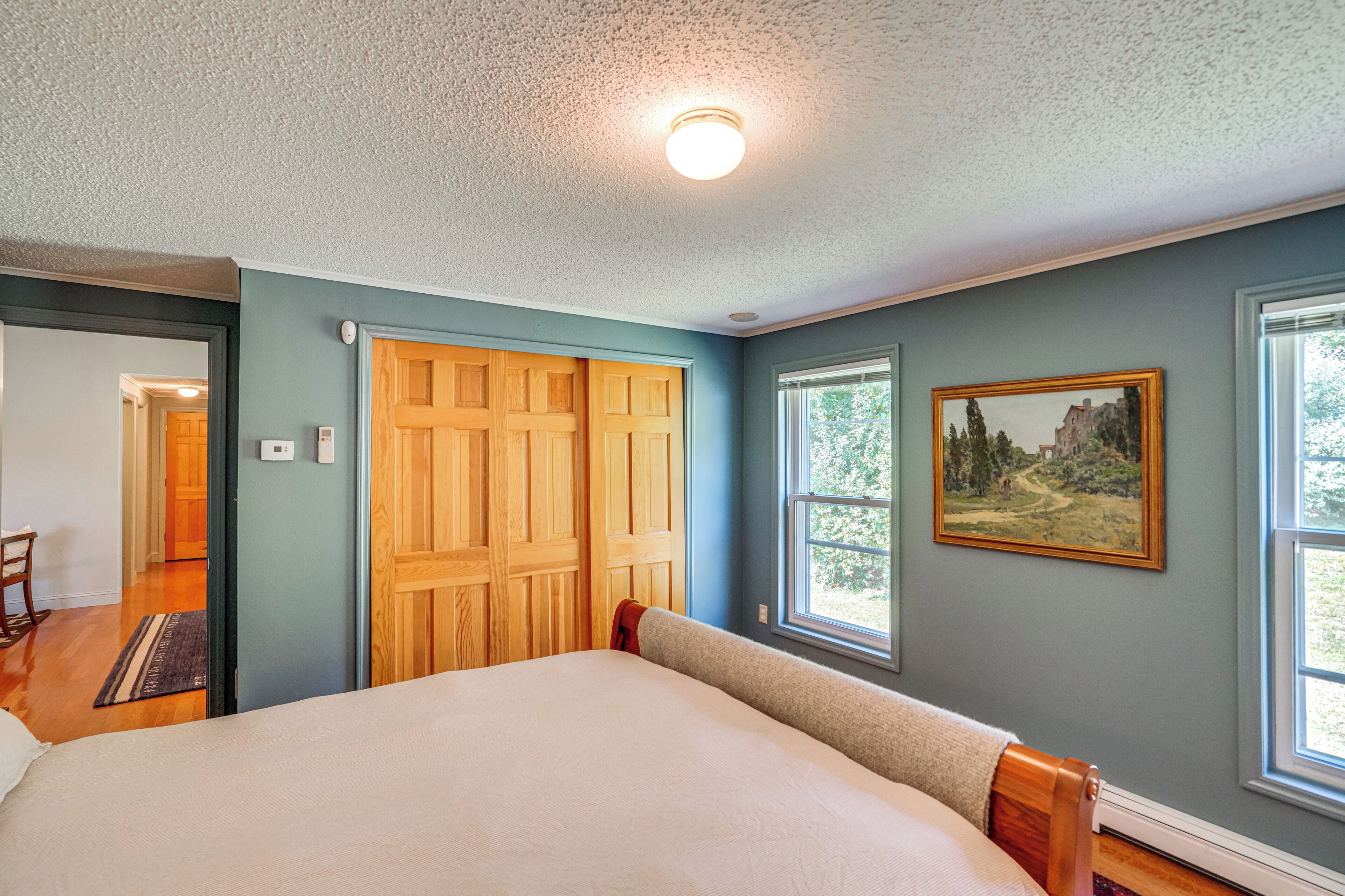 A bedroom with a large bed, wooden closet, and a painting on the wall.