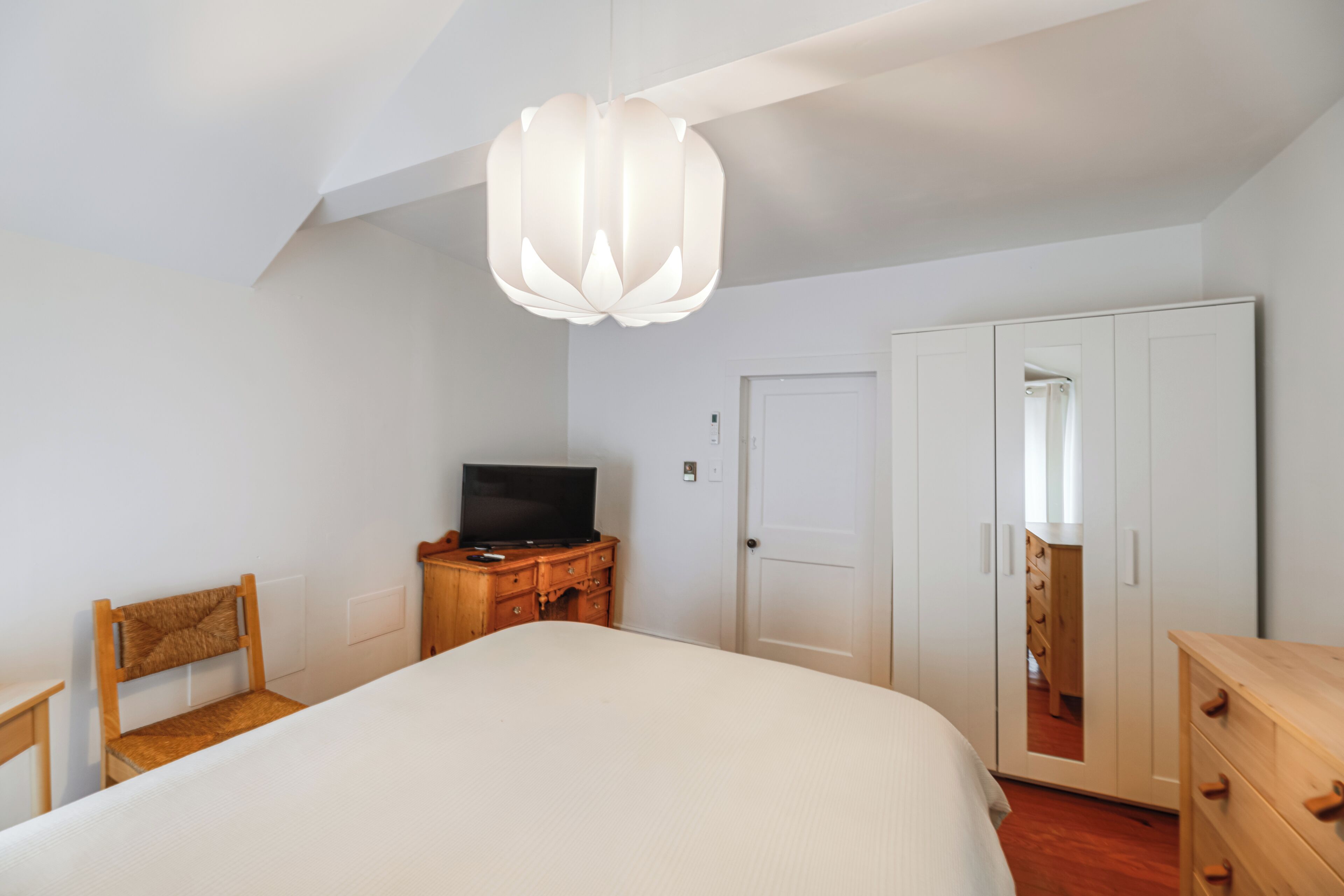 Une chambre à coucher comprenant un lit, une commode en bois, un téléviseur et une armoire.