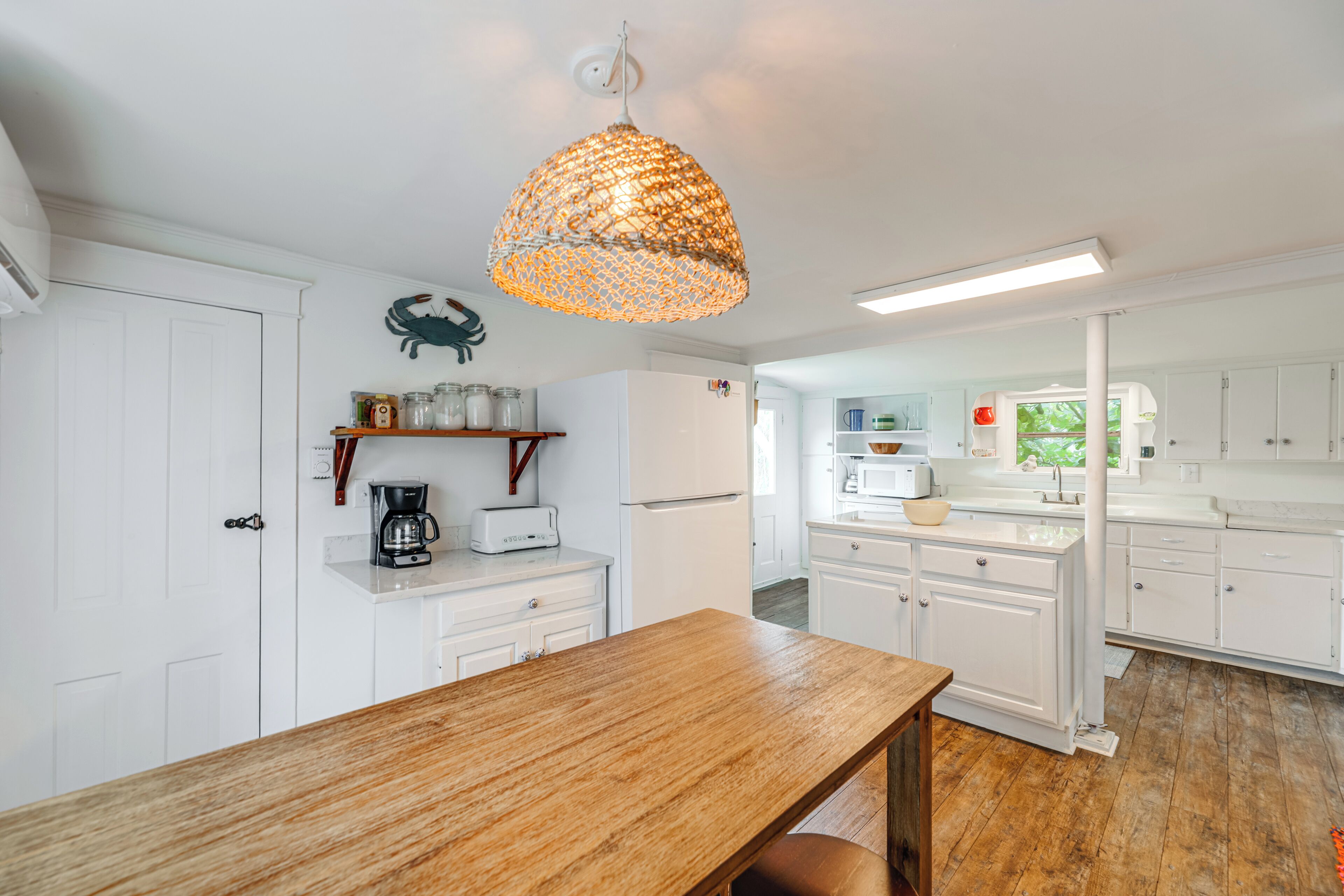 A modern kitchen with white cabinetry, a wooden dining table, and a hanging light fixture.