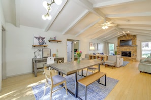 A spacious living area with a high ceiling, wooden flooring, a dining table with chairs, a sofa, a fireplace, and a TV mounted on the wall. - Home w/ Trail Access & Fire Pit in Bella Vista! (Bella Vista)