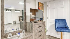 Ein Zimmer mit einem Holzschrank, einem großen Spiegel, einem blauen Stuhl und einer Tür.