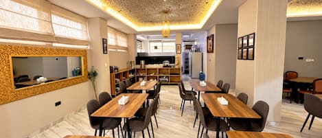 A modern dining area with wooden tables and chairs, a decorative ceiling, and a kitchen in the background.