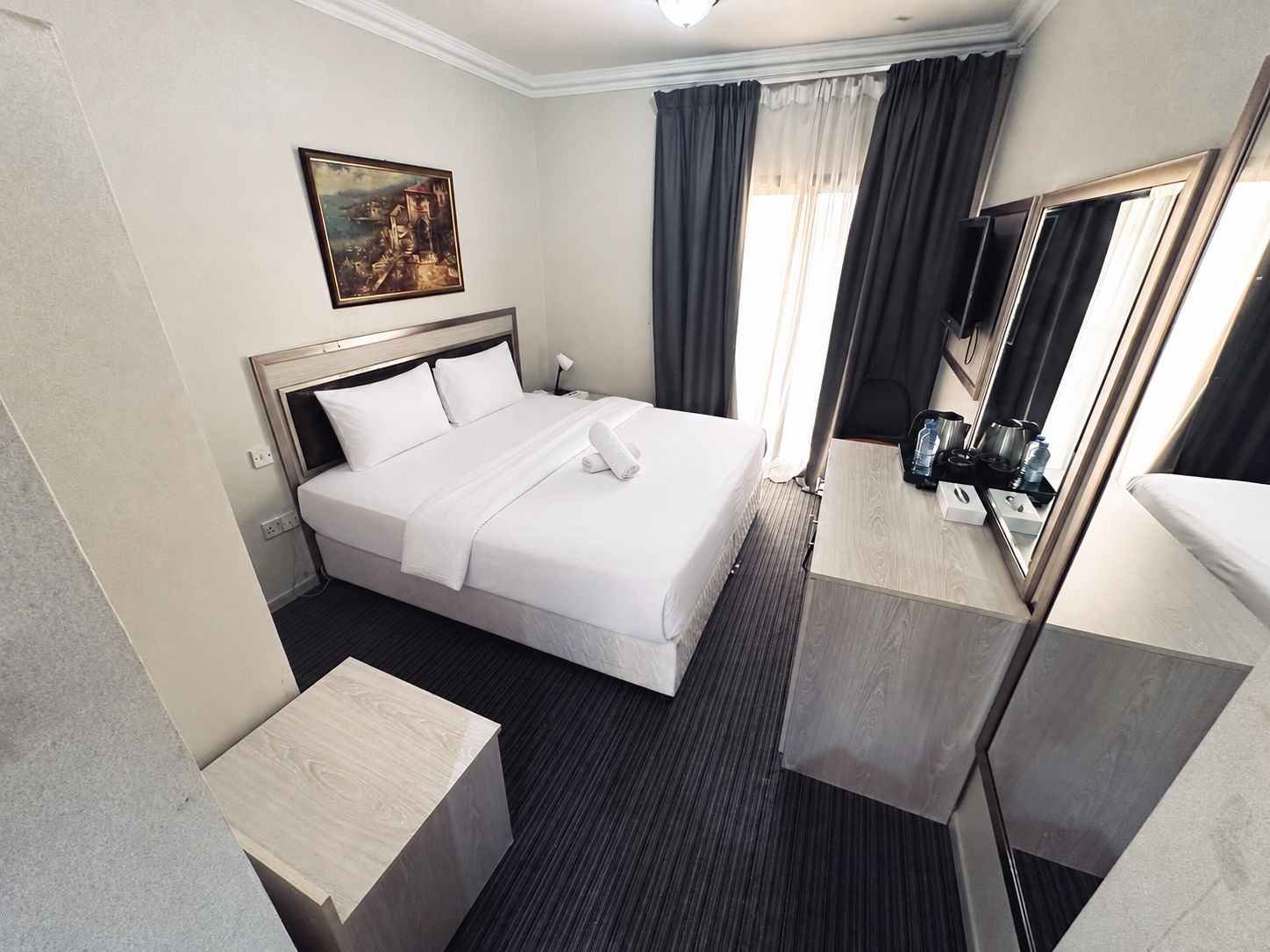 Habitación de hotel con cama, mesita de noche, espejo y un cuadro en la pared.
