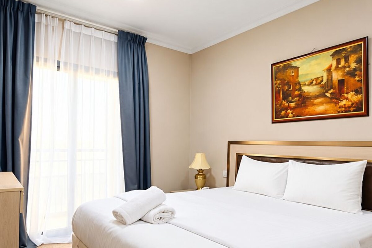 A hotel room with a large bed, a painting on the wall, and a window with curtains.