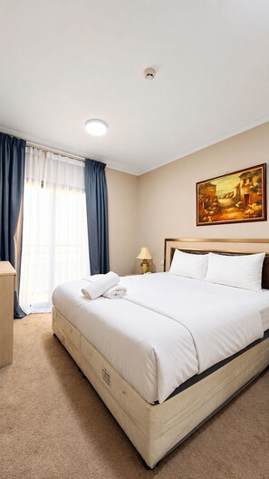 A hotel room with a large bed, a painting on the wall, and a window with curtains.