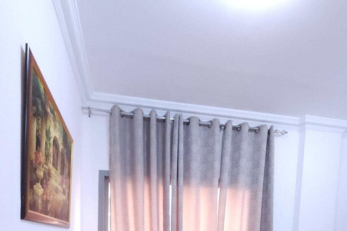 A neatly made bed with white linens, a grey headboard, and a painting on the wall.