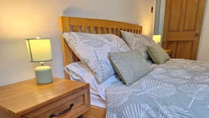 A neatly made bed with a leaf-patterned duvet, a bedside table with a lamp, and a wooden nightstand with a drawer. - Woodland View by the Canal Hebden Bridge (Hebden Bridge)