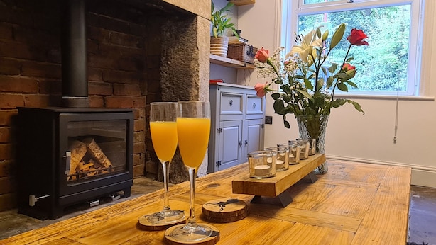 A cozy living room with a fireplace, a wooden table with two glasses of orange juice, and a vase with flowers. - Woodland View by the Canal Hebden Bridge (Hebden Bridge)