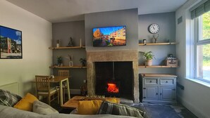 A cozy living room with a fireplace, a dining area, and a TV mounted above the fireplace. - Woodland View by the Canal Hebden Bridge (Hebden Bridge)