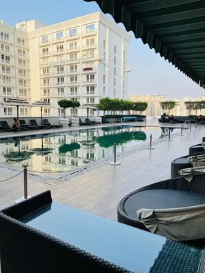 A rooftop pool area with lounge chairs and umbrellas, surrounded by a high-rise building. - Evanthe Hotel (Lucknow)