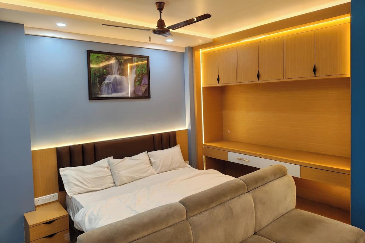 A modern bedroom with a bed, a ceiling fan, a wall-mounted TV, and built-in wooden shelving.