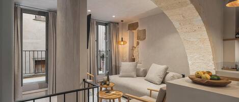 A modern interior with a stone archway, a cozy seating area with a sofa and armchairs, a wooden table, and a fruit bowl on a counter.