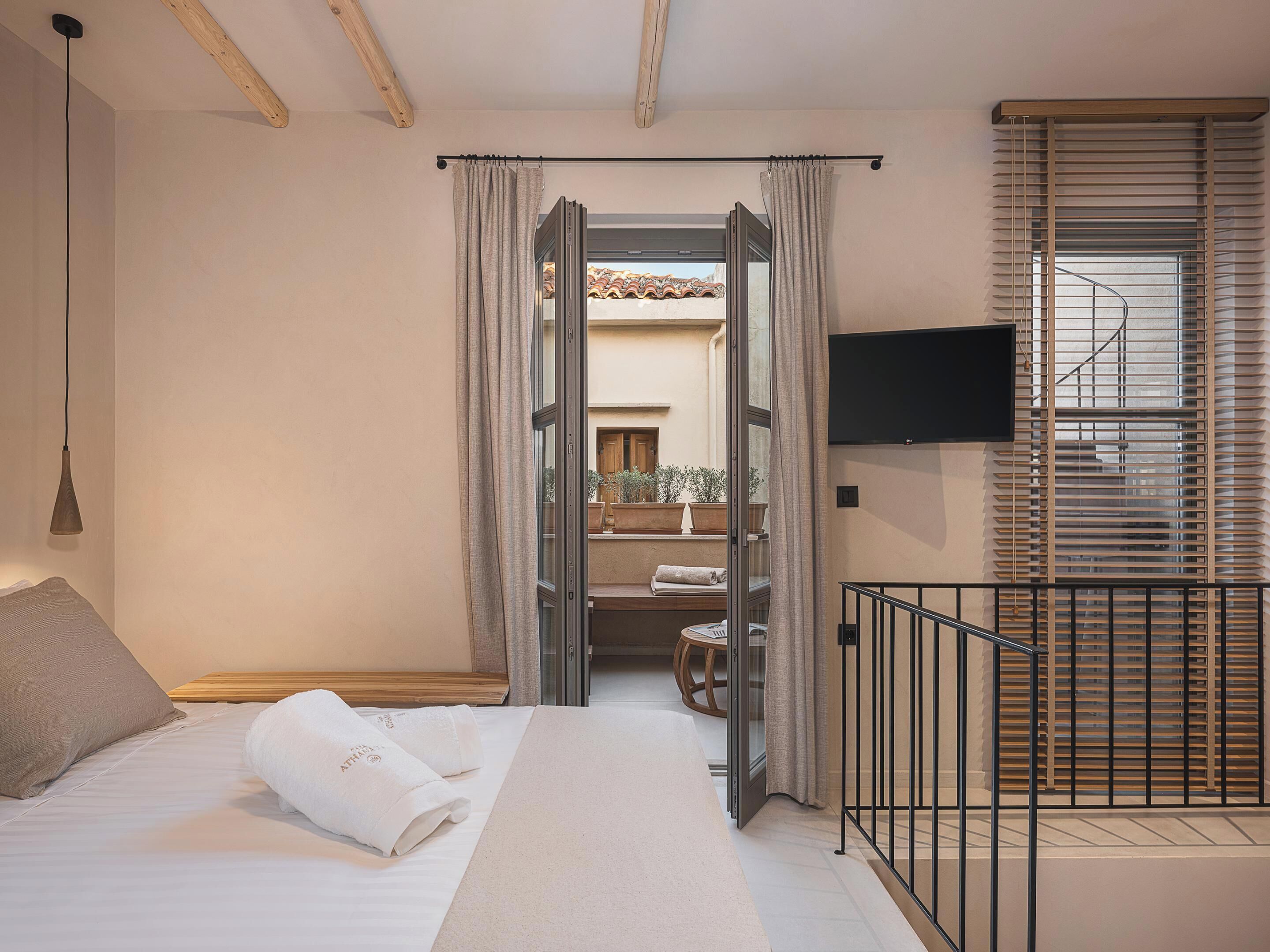 Habitación de hotel con cama, televisor montado en la pared y balcón con vistas al exterior.