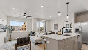 A modern kitchen with a large island, stainless steel appliances, and a dining area with a sofa and chairs. - Life is Good: Desert Color Lagoon + Beaches (St. George)