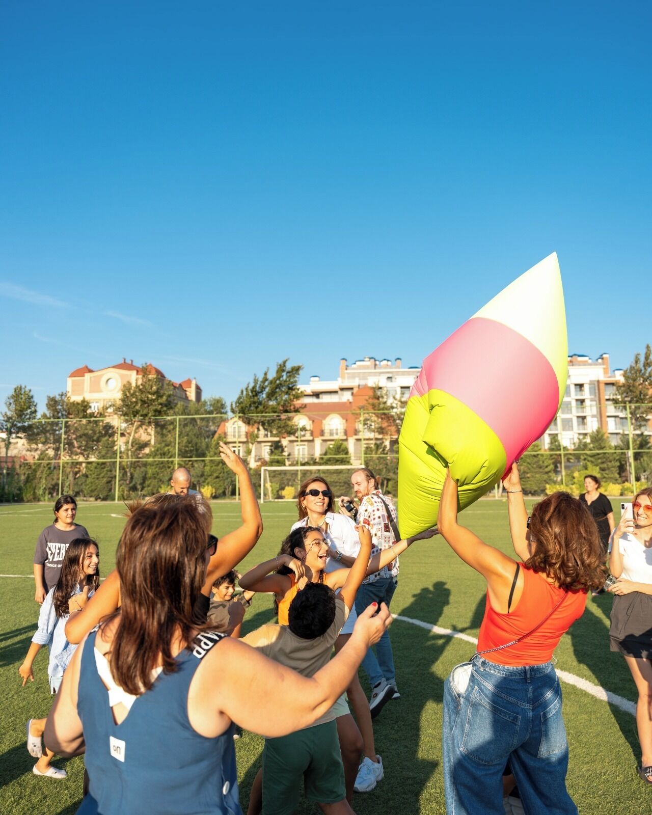 Un groupe de personnes se trouve sur un champ d’herbe, et certaines d’entre elles tiennent un grand objet coloré.
