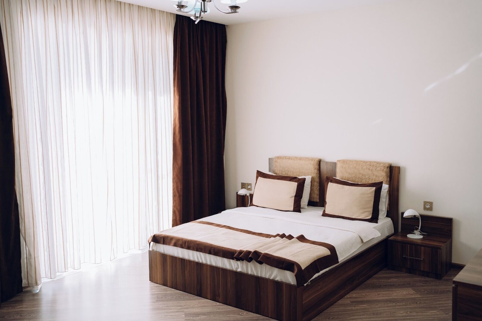 A modern hotel room with a large bed, wooden headboard, and a nightstand with a lamp.