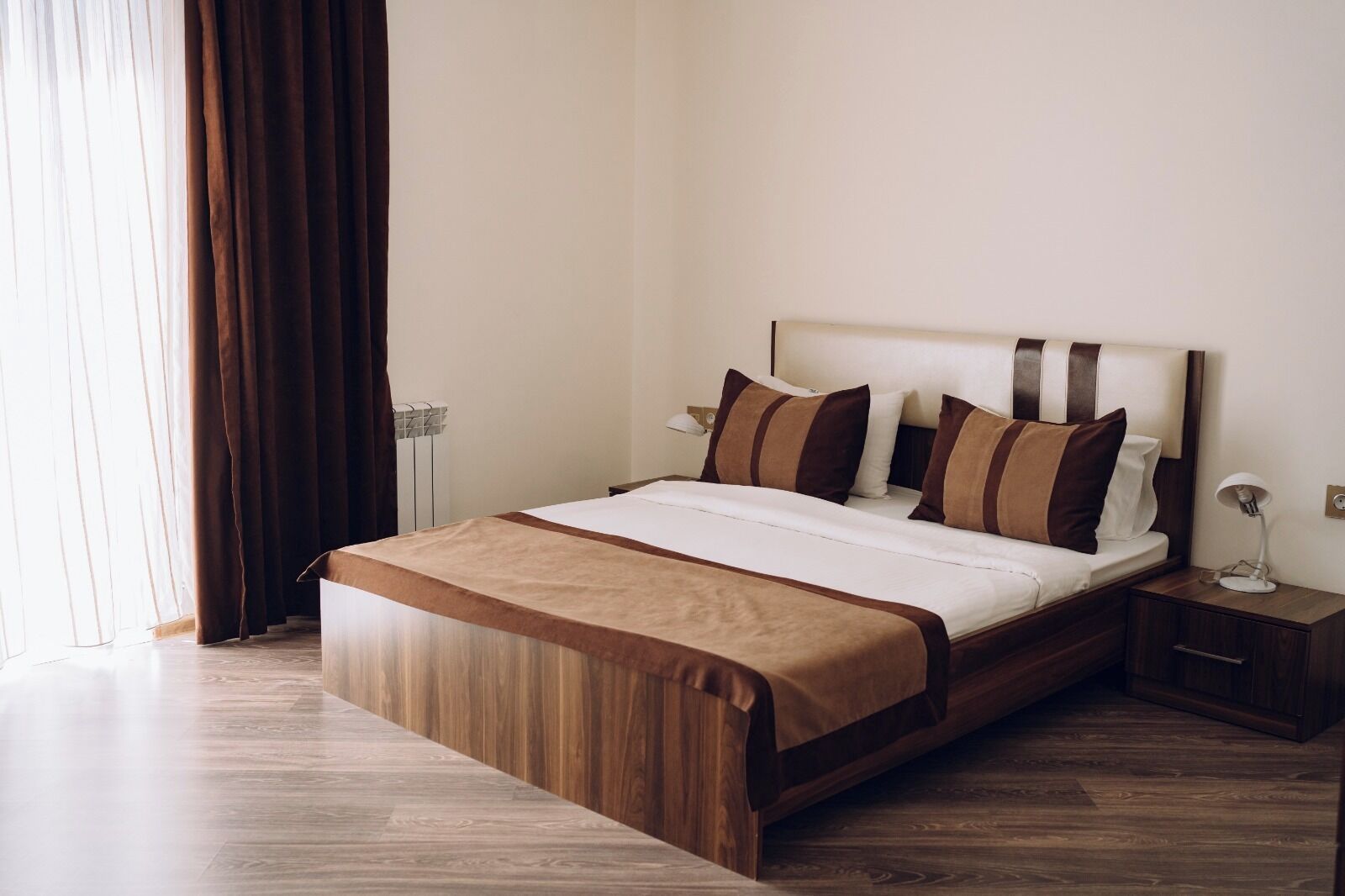 Une chambre d’hôtel avec un lit en bois, une table de chevet, une lampe et une fenêtre avec des rideaux.