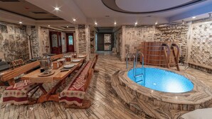 A spa area with a wooden pool, stone walls, and a dining setup. - Green City Resort (Baku)