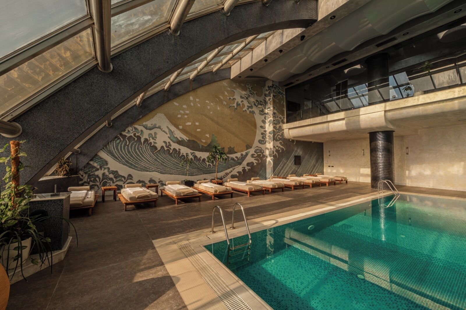 A modern indoor pool area with a wave-patterned wall, lounge chairs, and a clear pool.