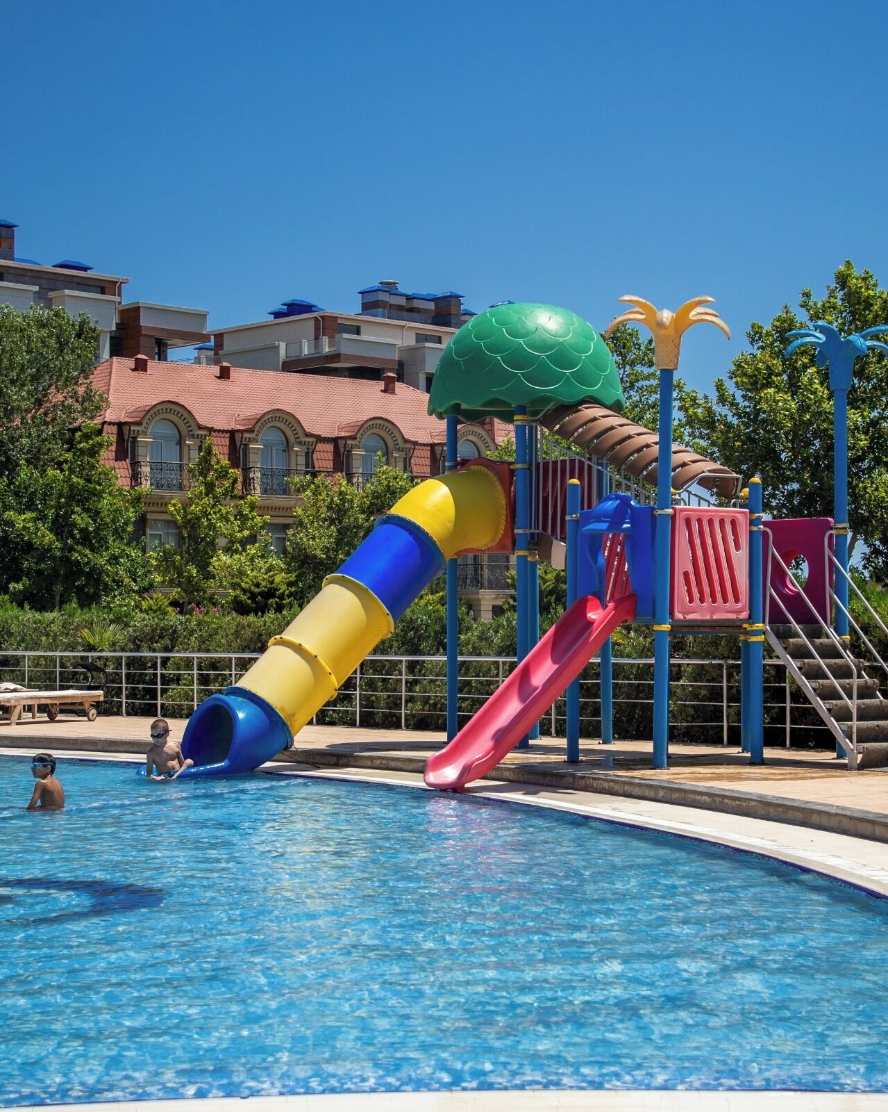 En swimmingpool med en färgglad vattenrutschkana och en grön, kupolformad konstruktion.