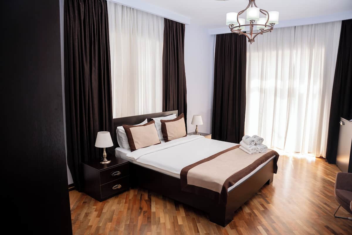 Una habitación de hotel con una cama grande, cortinas oscuras, una araña de cristal y suelo de madera.