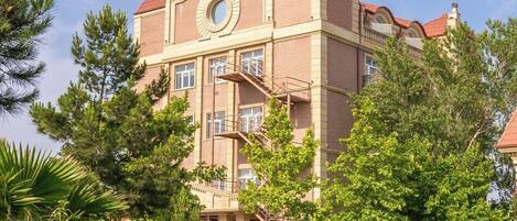 A multi-story building with a circular window on the second floor, surrounded by lush greenery and trees.