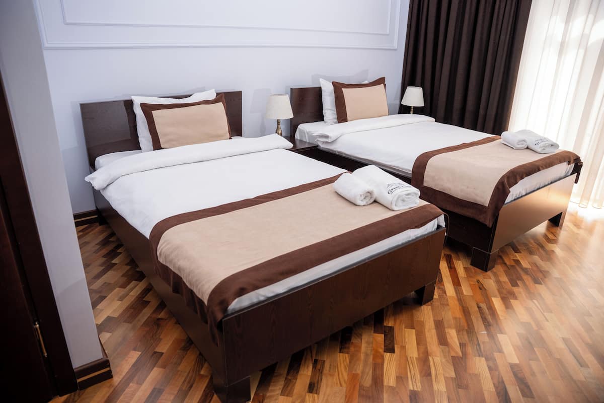 Habitación de hotel con dos camas, suelo de madera y una ventana con cortinas.