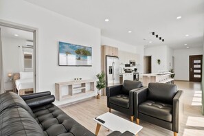 A modern living room with a sofa, armchairs, and a coffee table. There is a kitchen in the background with a refrigerator and microwave. - Home Oasis 3BR w Private Pool & Patio near Beaches (Oranjestad)