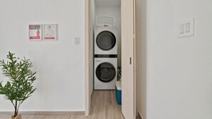 Een wasserette met twee gestapelde wasmachines, een mand bovenop en een blauwe prullenbak.