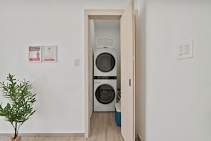 A laundry room with two stacked washing machines, a basket on top, and a blue trash bin. - Home Oasis 3BR w Private Pool & Patio near Beaches (Oranjestad)