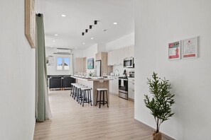A modern kitchen with a central island, bar stools, and a potted plant.