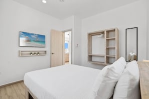 Een slaapkamer met een bed, een aan de muur bevestigde televisie, een houten plank met kleine planten, en een spiegel.