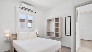 Een slaapkamer met een bed, nachtlampjes, een raam, een airconditioningapparaat, een houten garderobe en een deur.