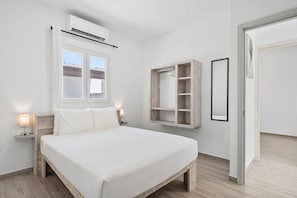 A bedroom with a bed, bedside lamps, a window, an air conditioning unit, a wooden wardrobe, and a door. - Home Oasis 3BR w Private Pool & Patio near Beaches (Oranjestad)