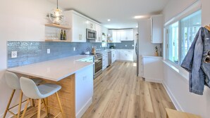 A modern kitchen with white cabinets, a large island, and a view of the outside. - The Peacock Place – Family Home w/Heated Pool (Tampa)