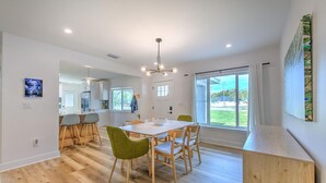 A modern kitchen with white cabinets, a dining area with a wooden table and chairs, and a large window offering a view of the outdoors. - The Peacock Place – Family Home w/Heated Pool (Tampa)