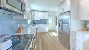 A modern kitchen with white cabinets, a stainless steel refrigerator, and a wooden countertop. - The Peacock Place – Family Home w/Heated Pool (Tampa)