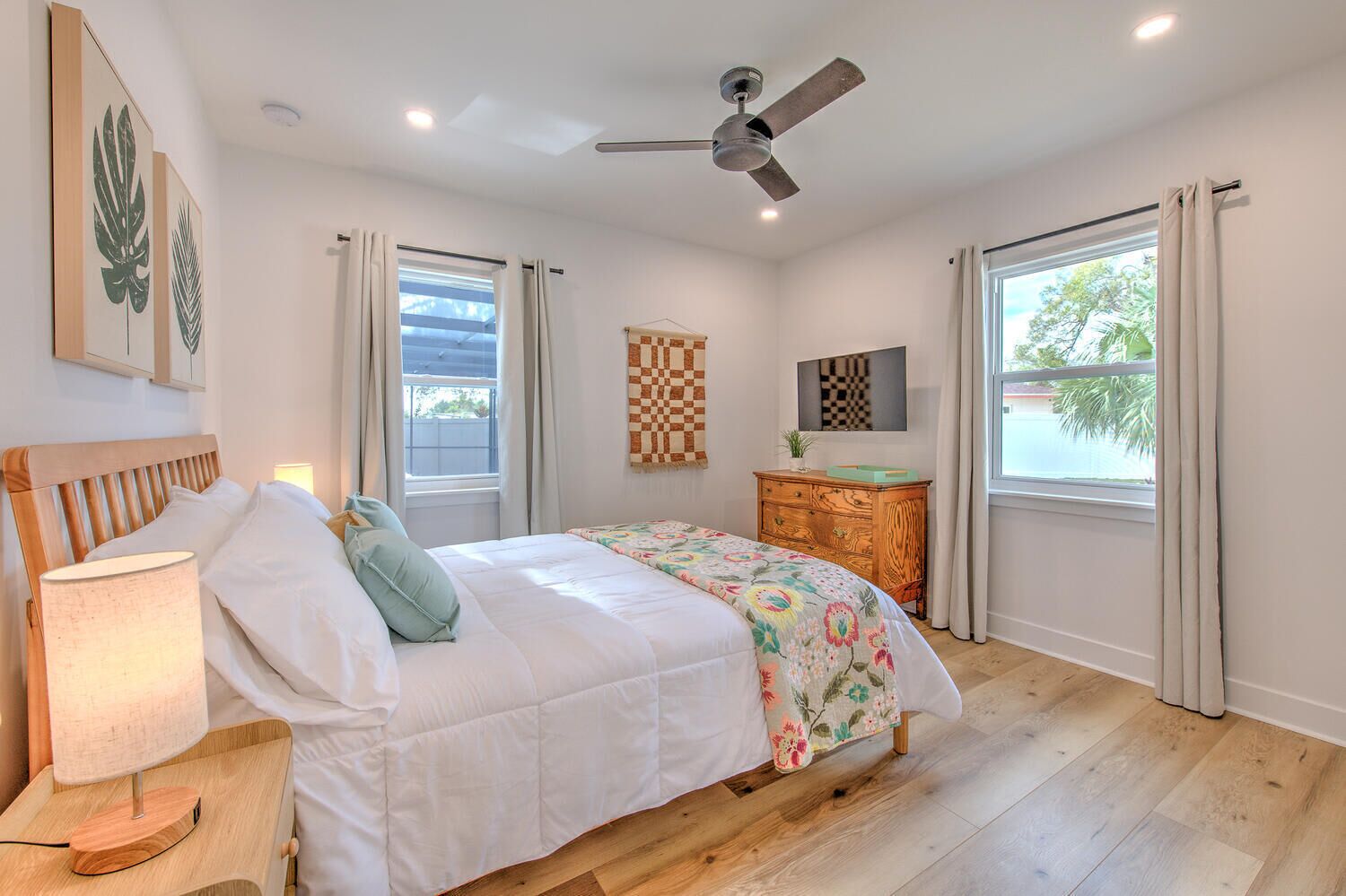 A bedroom with a bed, a wooden nightstand, a ceiling fan, a dresser, and a window with curtains.