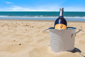 Una botella de champán en un enfriador portátil en una playa, con el océano al fondo.