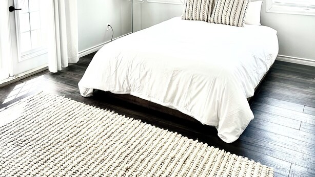 A bedroom with a large bed, a white rug, a wall sign that says "BEACH", and a window with blinds. - Our Happy Place: Hot Tub & Trail Access: STR25-00043 (Tory Hill)