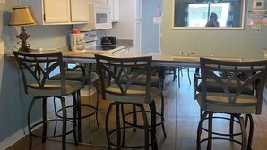 Une cuisine avec des meubles blancs, un îlot central doté de tabourets, et une fenêtre donnant sur l’extérieur.