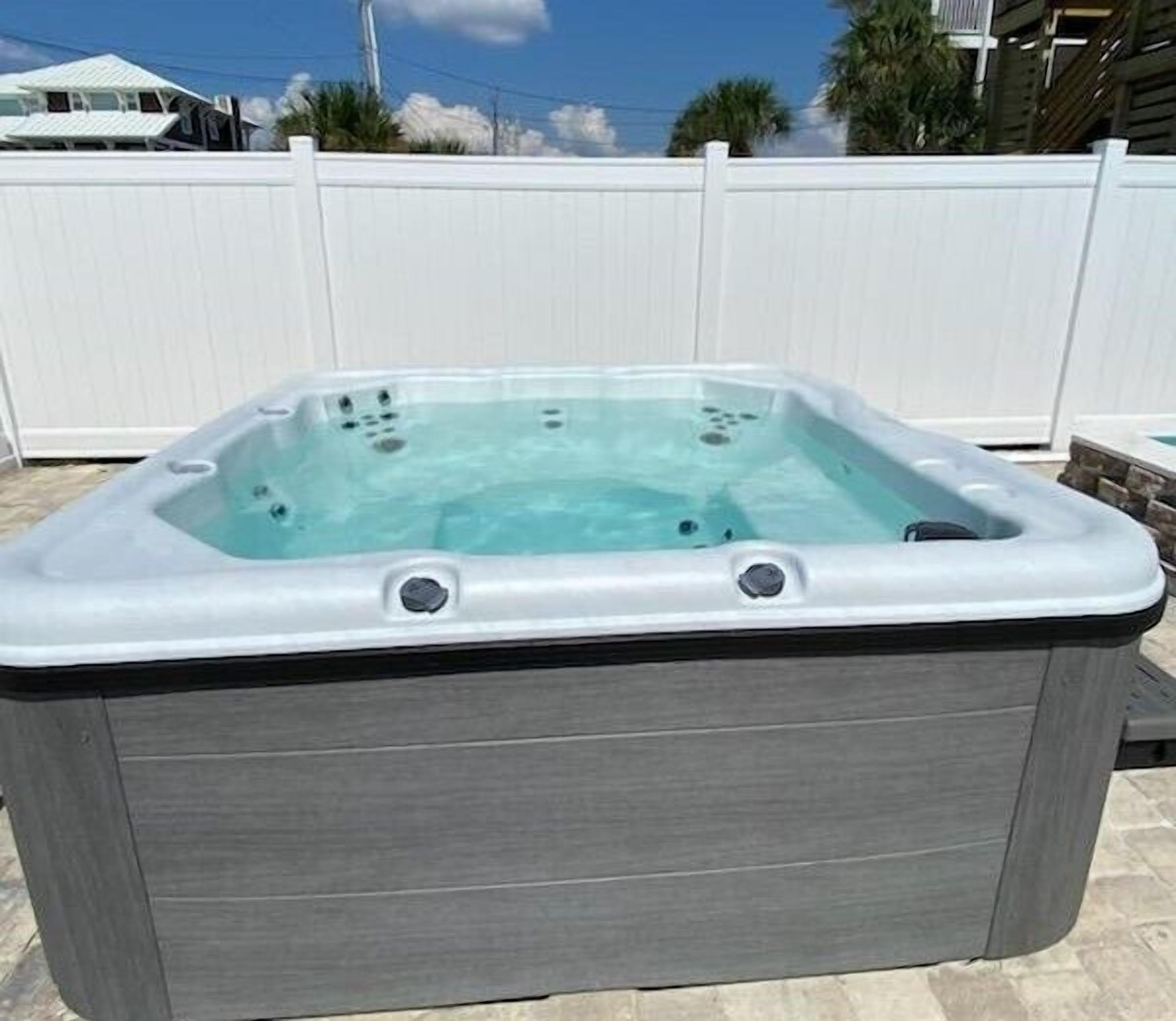 A rectangular hot tub with a white interior and gray exterior, positioned outdoors with a white fence in the background.