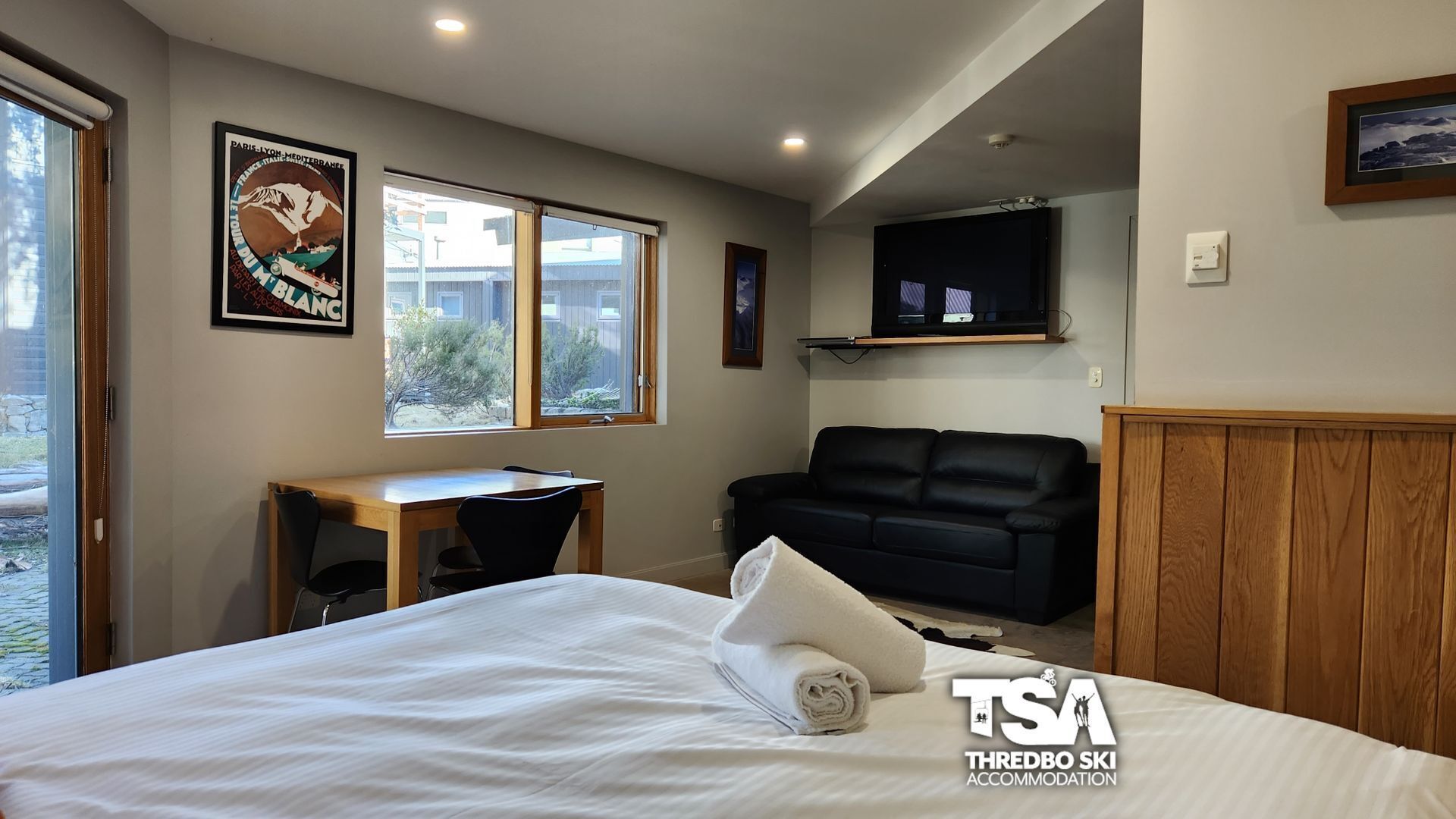 Une chambre à coucher comprenant un lit, un bureau, un canapé en cuir noir et un téléviseur fixé au mur.