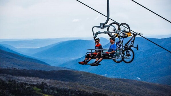 Two people seated on a cable car with a bicycle rack, overlooking a mountainous landscape. - Powder 3A - Woodridge (Woodridge)