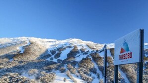 Un letrero con el nombre 'THREDBO' en una zona montañosa con terreno nevado.