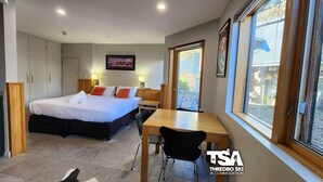 Un dormitorio con cama, mesitas de noche, un escritorio y una silla. Se ve una ventana con vistas al exterior.