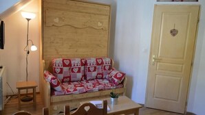 Een gezellige kamer met een houten bank bekleed met kussens met een hartpatroon, een klein houten tafeltje, een vloerlamp en een gesloten deur met een hartvormige decoratie.