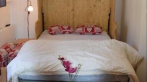 Een gezellige slaapkamer met een houten hoofdbord, een nachtkastje met een boek en een plant, en een lamp aan de muur.