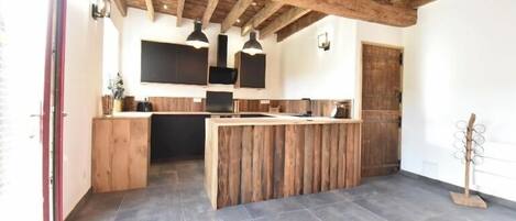 Una cocina rústica con vigas de madera, una isla central, iluminación colgante y piso de baldosas.