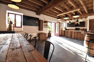 Un coin repas rustique avec une table et des chaises en bois, un espace cuisine doté de meubles en bois et une grande fenêtre laissant entrer la lumière naturelle.